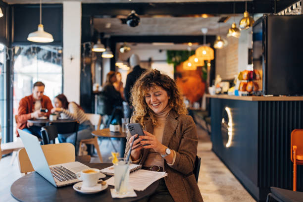 istock Smiling female entrepreneur enjoying a coffee break at a table in a coffee shop, using her smartphone to browse the internet. Businesswoman using coffee shop to work remotely 2191172583