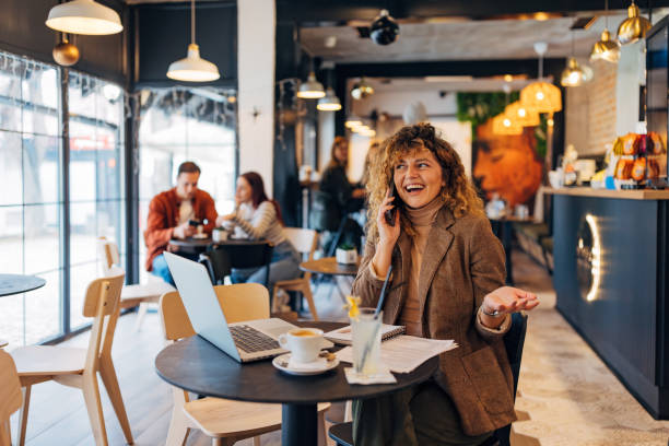 istock Carefree female entrepreneur talking on mobile phone while sitting at the table in front of laptop during  coffee break in coffee shop 2191172617