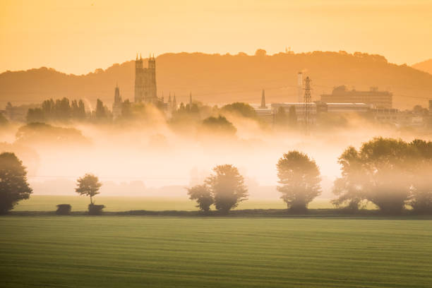 View over misty morning valley to distant city and cathedral silhouetted by the golden light of sunrise.