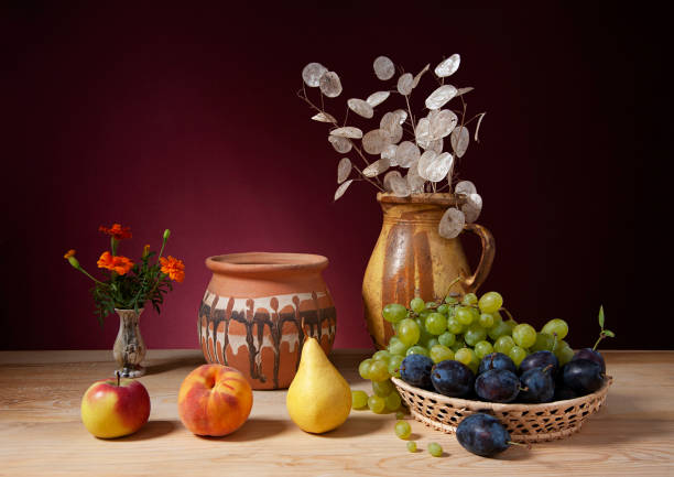 Still life, ceramic jug, ceramic pot, flowers and various fruits on a wooden table