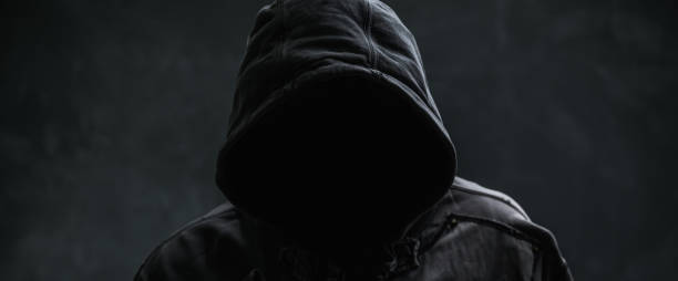 istock Unrecognizable cyber criminal or computer hacker wearing black hooded jacket, low key portrait 2191180219