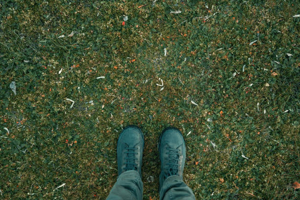 Standing on lush green grass meadow ground, feet with boots from above, top view