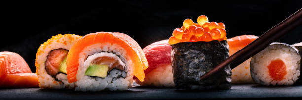 istock Sushi rolls panorama on a black background. Ikura maki roll with chopsticks 2191182353