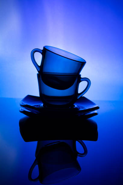 Set of Two Glassed Teacups or Coffee Cups With Plate Isolated Over Glowing Blue Gradient Background. Vertical Shot