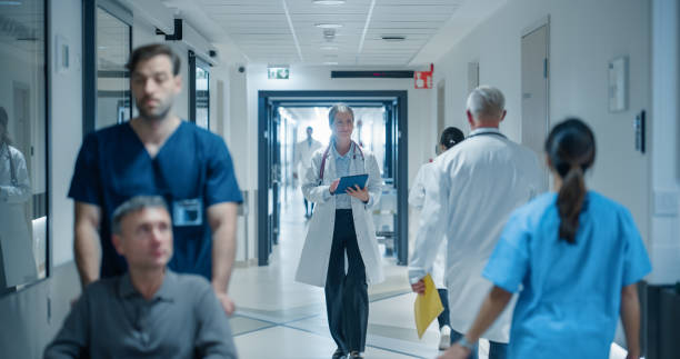istock Diverse Medical Staff Walking Down a Hospital Hallway, Each Headed Towards Different Departments. Caucasian Female Doctor Discussing Treatment Plans, Reviewing Patient Charts on a Tablet 2191184067