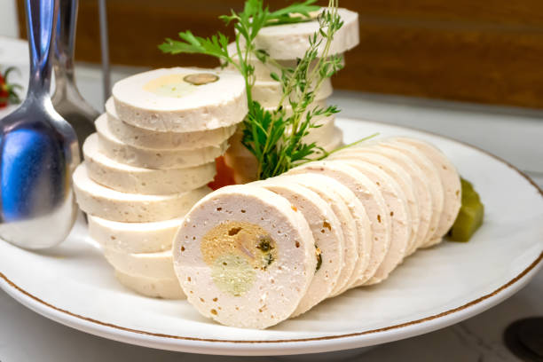 Close-up image of home-made chicken mortadella served with olives and ham slices. The dish is presented in a restaurant-style setting.