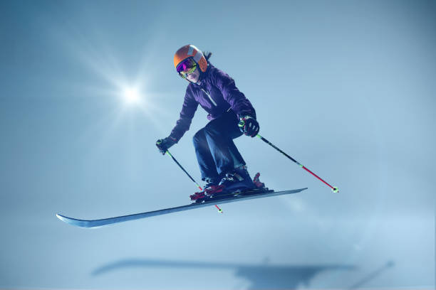 Winter athlete launching dynamically, orange helmet and reflective goggles glinting under studio lighting, emphasizing speed against seamless blue. Concept of extreme sport, Christmas holidays. Ad