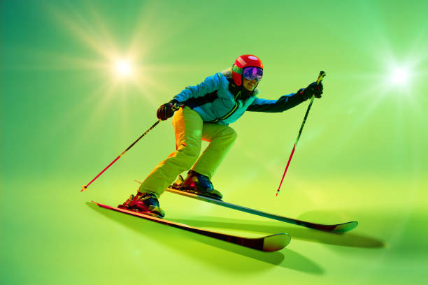 Side view, low angle of athletic woman, skier gliding forward against intense green studio background in neon green ambiance.