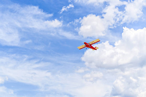 Red single-engine ultralight airplane flying in the blue sky with white clouds