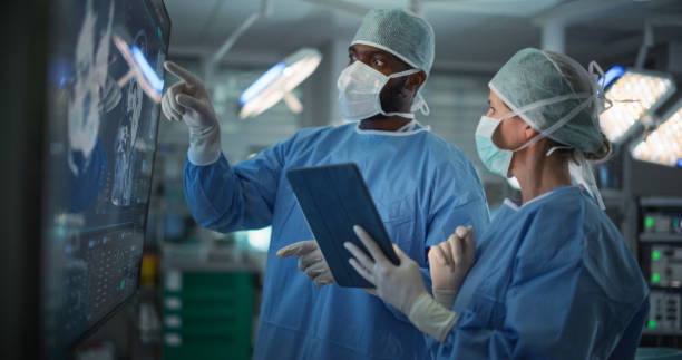 istock Diverse Colleagues Having a Discussion In the Operating Room. Female and Male Surgeons Evaluate Complex Brain Scans on a Large Display, Strategizing the Next Steps for the Operation 2191191663