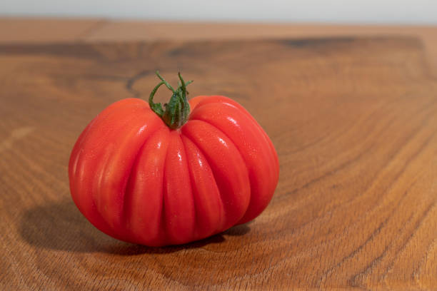A vibrant red ripe tomato positioned on a clean white background. Showcasing its natural texture and leafy green stem, this image highlights the fresh, organic essence of the fruit, commonly associated with healthy eating, gardening, and culinary ingredients. Perfectly lit, it conveys freshness and vibrancy.