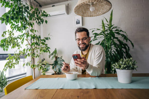 istock A man using his phone while enjoying a bowl of cereal for breakfast in a cozy morning setting 2191198331