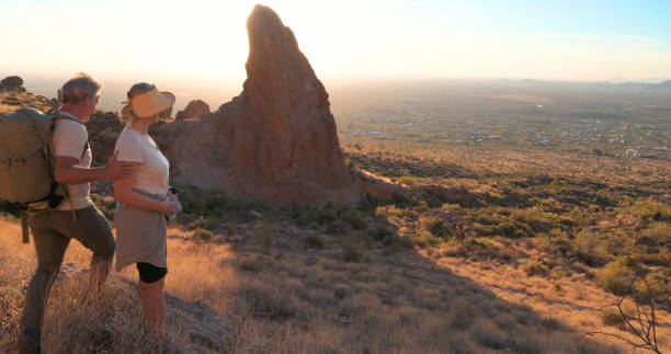 Mature couple hike below rock spire at sunset, Apache Junction, AZ