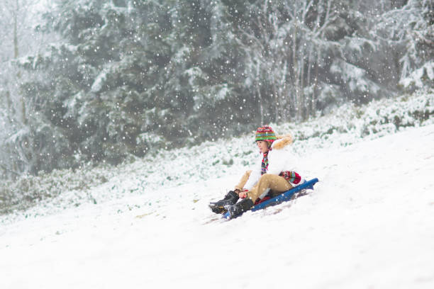 Young woman falling in snow after sledding down a hill on a sunny winter day