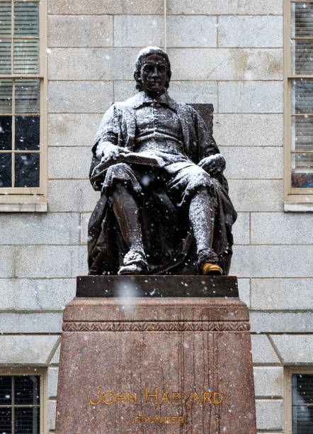 Cambridge, Massachusetts, USA - December 20, 2024: Close-up of snow falling on the John Harvard statue in Harvard University's Harvard Yard. The John Harvard monument (c. 1884) is a bronze statue of John Harvard (1607-1638) by Daniel Chester French. The monument inscription is \