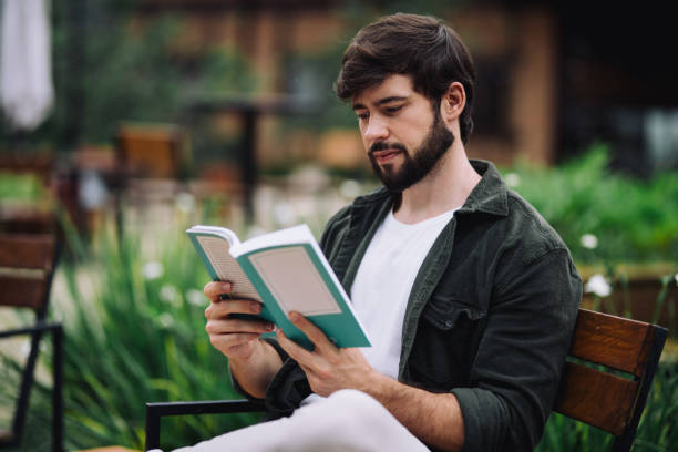 istock Side view of young man reading a book at a public park 2191210390