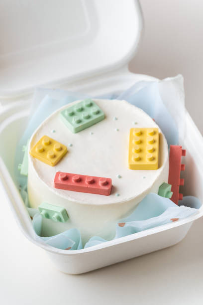 Little plastic building blocks style cake in a gift bento box. Birthday cake decorated with colorful chocolate construction blocks on the white background