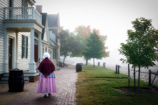 Williamsburg, Virginia, USA - October 23, 2024: A woman, in period cloting, walks down Duke of Gloucester street on a foggy day at the historic colonial district.