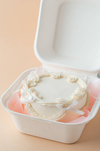 istock Delicate small lambeth style cake with white cream cheese frosting in a gift bento box. Cake as a gift for a beloved one. Spring tender cake for a woman on the beige background. Top view 2191215400