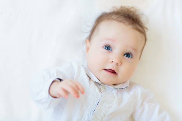Adorable baby in white sunny bedroom. Newborn child relaxing in bed. Nursery for young children. Textile and bedding for kids. Family morning at home. Child in knitted sweater.
