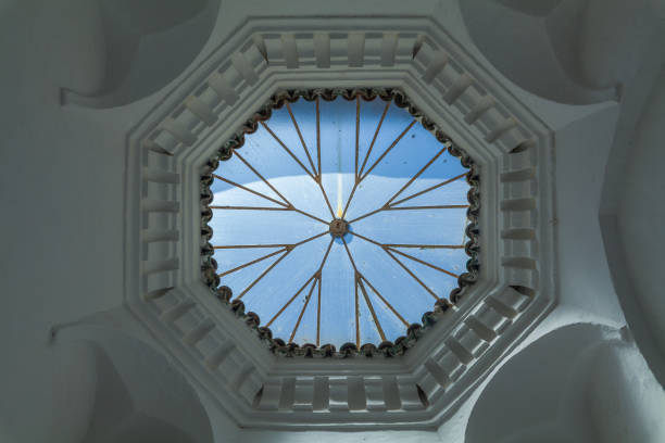 architectural detail with a circular skylight featuring a geometric pattern and radiating glass panes, casting a beautiful interplay of light and shadow on the surrounding white walls