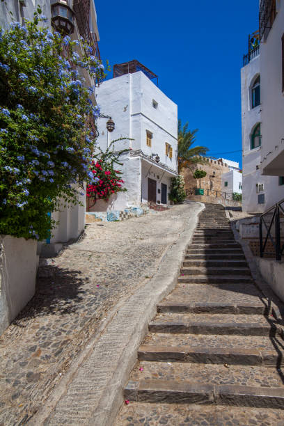istock charming, narrow street ascending a hill in a Mediterranean town, featuring whitewashed buildings, colorful flowers, and a clear blue sky 2191228100