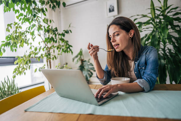 istock A woman is sitting at a wooden table in a cozy dining room while having breakfast and using a laptop 2191237708
