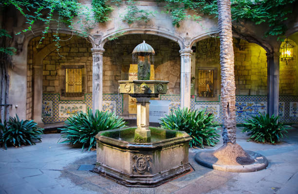 Barcelona, Spain - September 1, 2016 - A photo of an old, octagonal fountain surrounded by arched columns,  green foliage, decorative tiles and interesting wall lamps in the Picasso Museum on a summer morning in the Gothic Quarter of Barcelona, Spain.