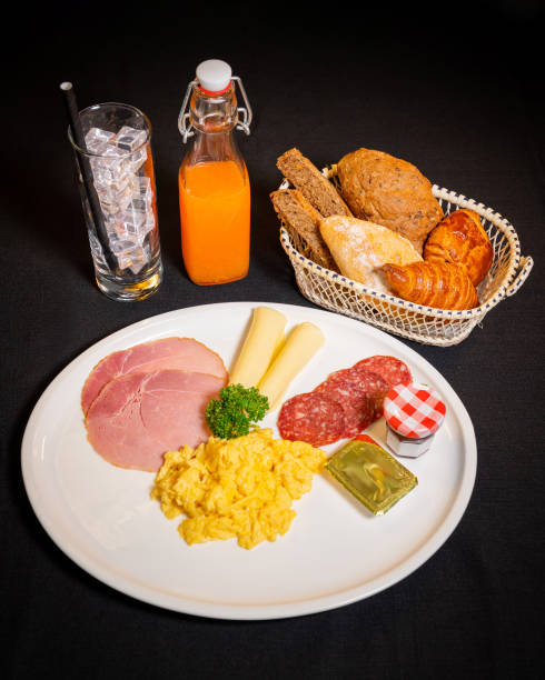 istock Breakfast spread on a plate, include scrambled eggs, slices of ham, salami, cheese sticks, and a small jar of jam 2191245816