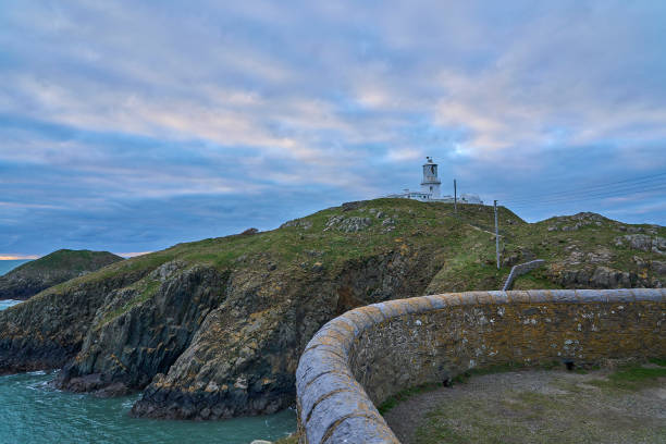 White Strumble Head lighthouse atop a rocky cliff overlooking a vast blue atlantic ocean in Pembroke Shire, Wales.