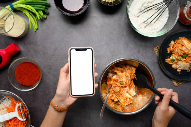 istock Hand holding smartphone while preparing Kimchi on a dark countertop surrounded by fresh ingredients and spices 2191256314