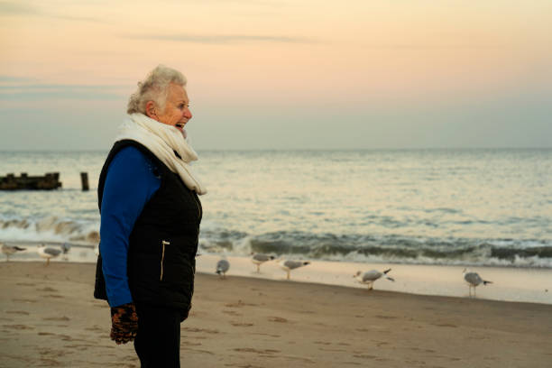 Senior woman smiles at the seagulls on Rehoboth Beach on a cold day, Dover, Rehoboth, Delaware