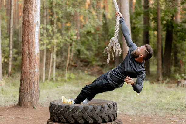 A middle aged male athlete of Caucasian descent sits on the turf ground, throwing battle ropes while working out in his backyard on a Florida day.
