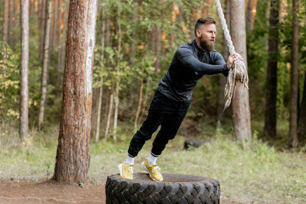 istock Stylish bearded man athlete doing training with rope holding it with hands. Training among trees, in forest 2191267540