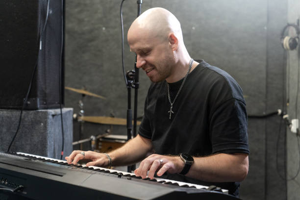 istock Sound producer working on new hit in recording studio, playing keyboard with focused expression. Professional environment with drums, microphone, and sound equipment 2191272934
