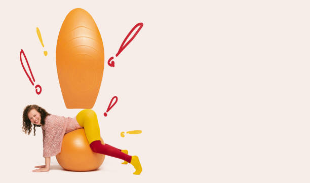 istock Cheerful woman balancing on orange exercise ball with exaggerated exclamation marks for creative, playful mood. 2191274223