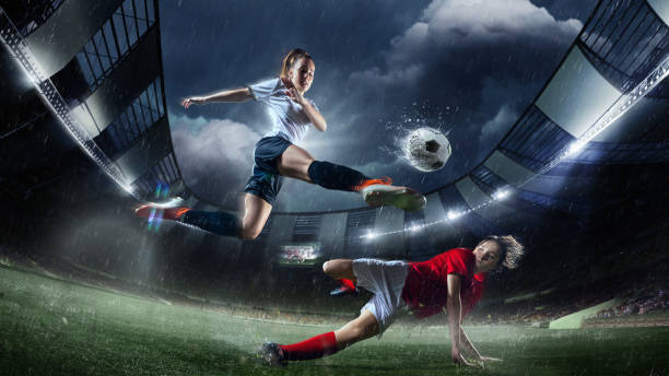 istock High-action soccer moment featuring female player in white performing powerful kick over player in red. Rainy 3D-modeled stadium. 2191274422