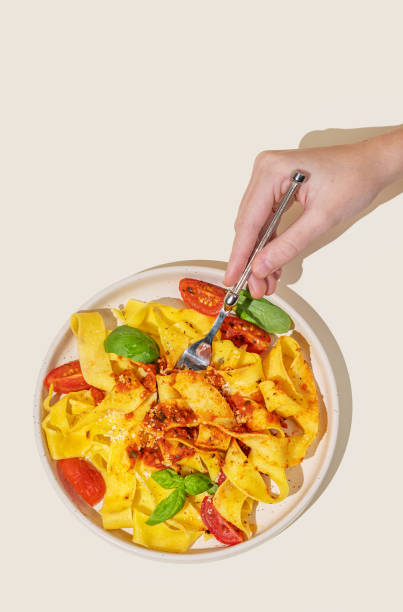 istock Hand holding fork with tagliatelle or pappardelle pasta with tomato sauce, basil and parmesan cheese in plate on yellow background 2191276089