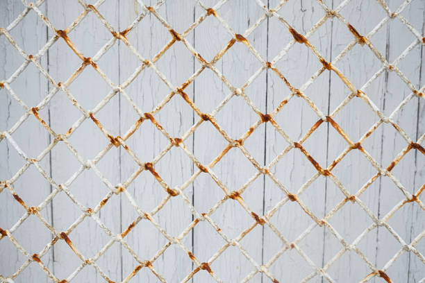 The texture is metal mesh paint. The old grid has a white rusty background. An abstract, authentic design background. A fragment of a fence, a time-aged close-up. Red streaks of rust on the metal