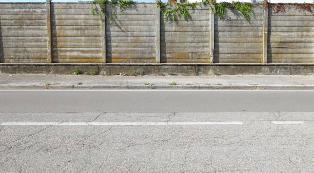 istock Old concrete precast compound wall with moss and ivy on top. Sidewalk and road in front 2191280516