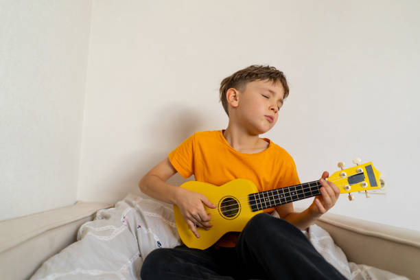 istock Boy playing a yellow ukulele while in his room at home 2191281561