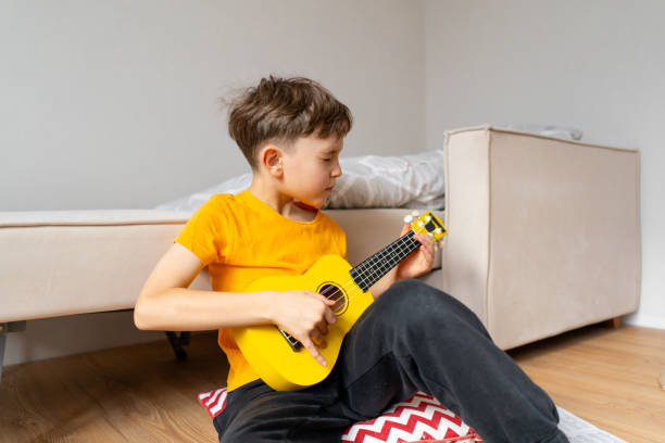 istock Boy playing a yellow ukulele while in his room at home 2191281578