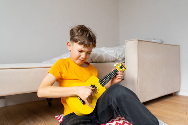 istock Boy playing a yellow ukulele while in his room at home 2191281593
