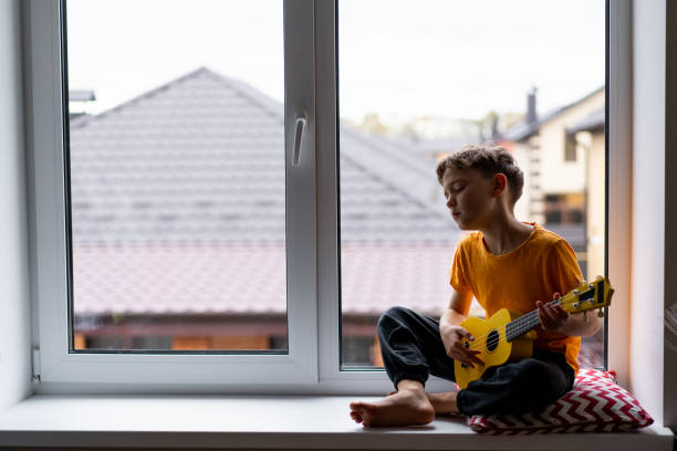 istock Boy playing a yellow ukulele while in his room at home 2191281598