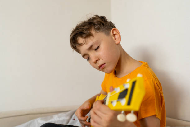 istock Boy playing a yellow ukulele while in his room at home 2191281612