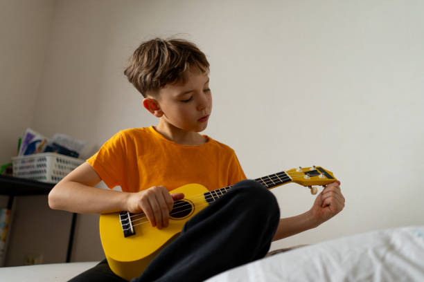 istock Boy playing a yellow ukulele while in his room at home 2191281623