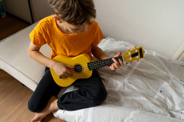 istock Boy playing a yellow ukulele while in his room at home 2191281720