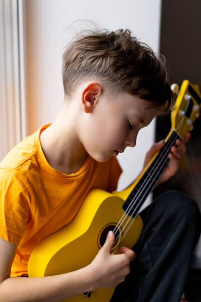 istock Boy playing a yellow ukulele while in his room at home 2191281723