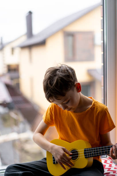 istock Boy playing a yellow ukulele while in his room at home 2191281771
