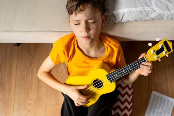 istock Boy playing a yellow ukulele while in his room at home 2191281774